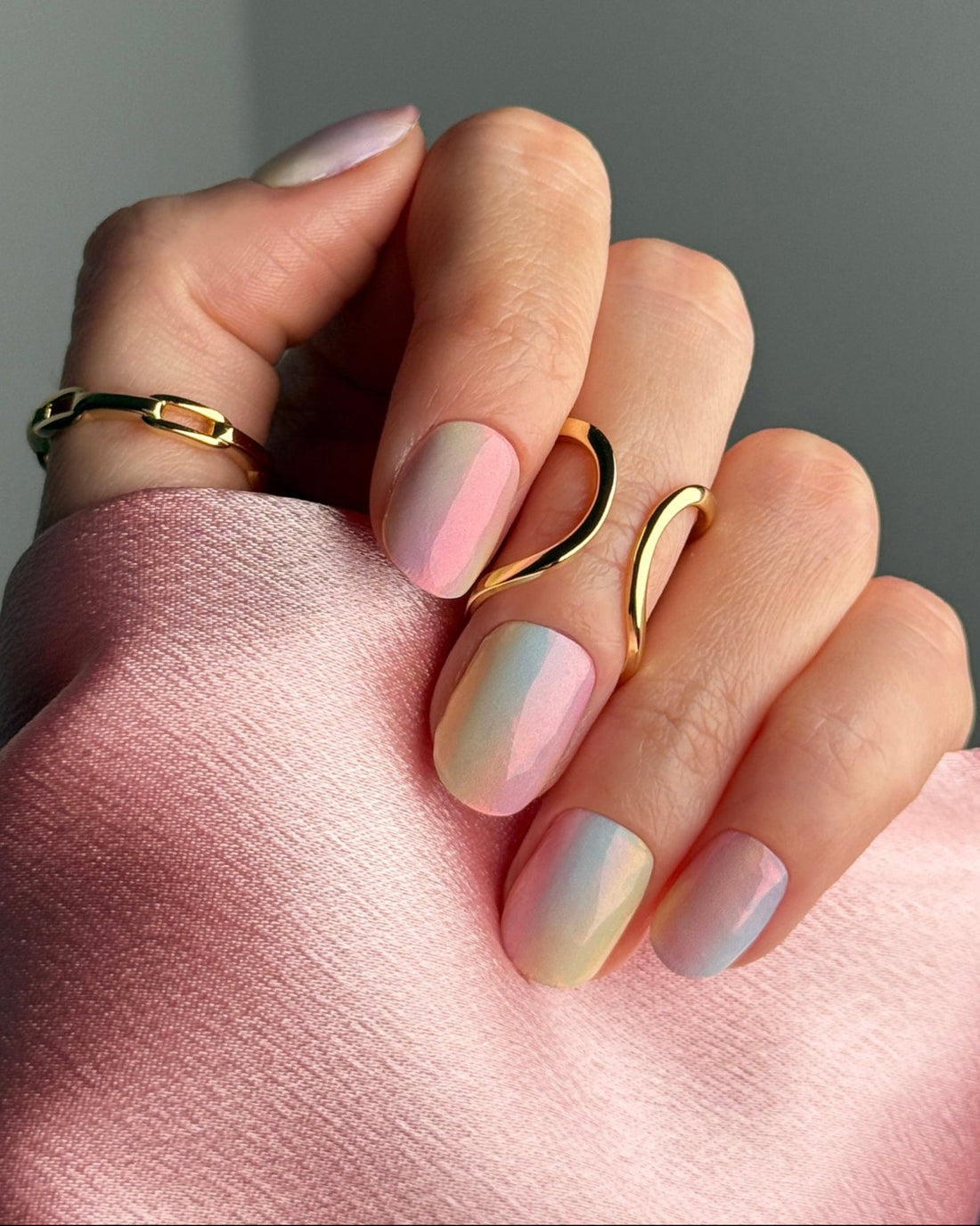 Hand model of semicured gel stickers with watercolor gradient design featuring shades of pink, blue, and yellow with a shimmer finish.